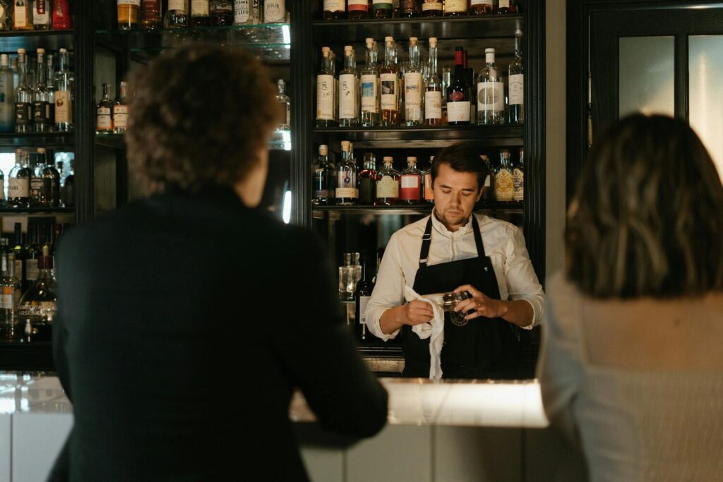 Bartender polishing a glass behind a bar with liquor bottles in the background