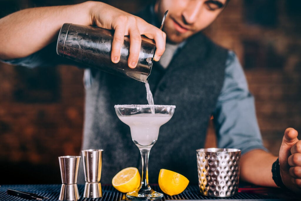 Bartender pouring a cocktail into a margarita glass