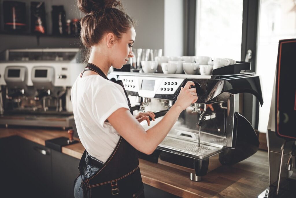 Young woman barista preparing coffee using machine in the cafe